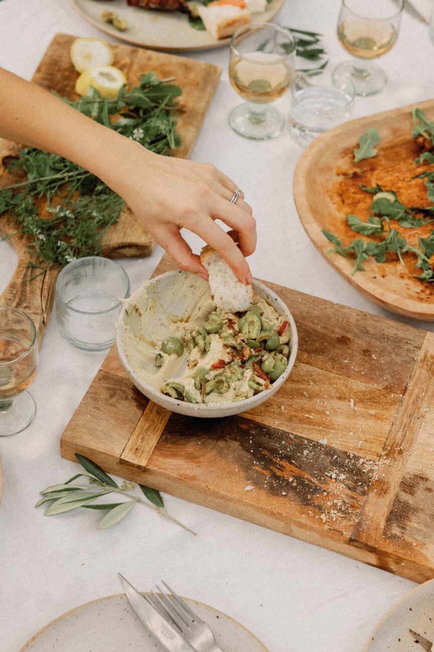 dipping bread into marinated olives with hummus