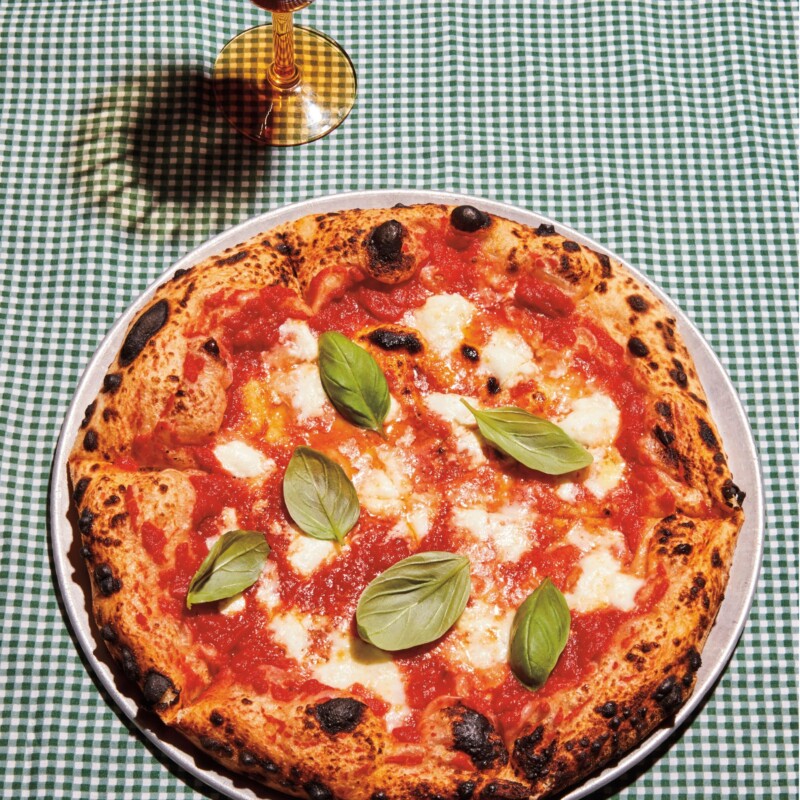 Full Margherita pizza on green checked gingham tablecloth.