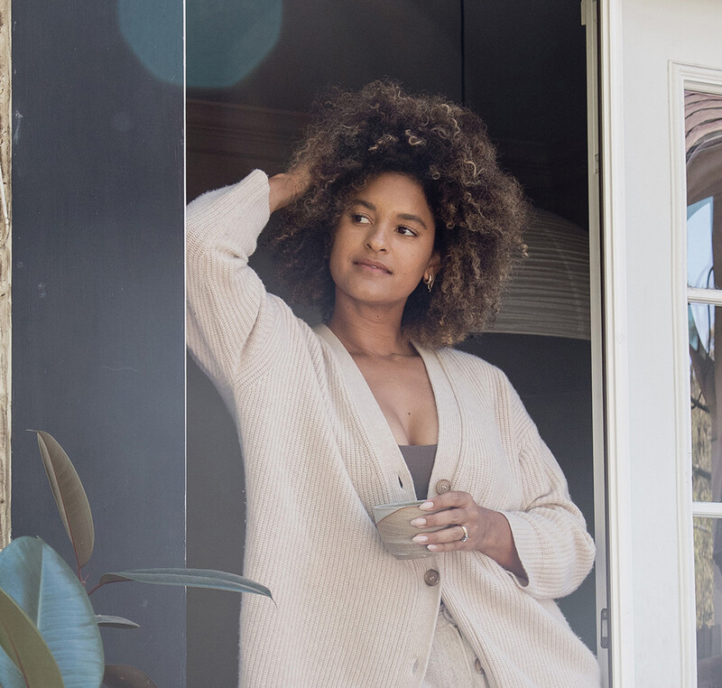 Black woman standing outside with cup of coffee.